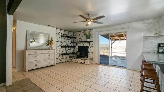 tiled living room featuring a wood stove and ceiling fan