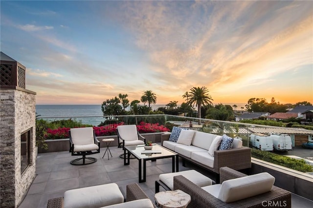 patio terrace at dusk with a water view and an outdoor living space with a fireplace