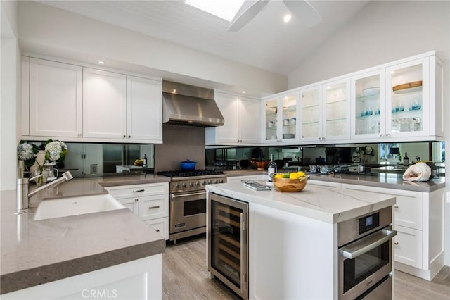 738 Cliff Dr, Laguna Beach, CA 92651 - kitchen featuring wall chimney exhaust hood, beverage cooler, appliances with stainless steel finishes, lofted ceiling, and white cabinets