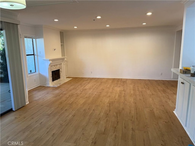 unfurnished living room with a premium fireplace, crown molding, and light hardwood / wood-style floors