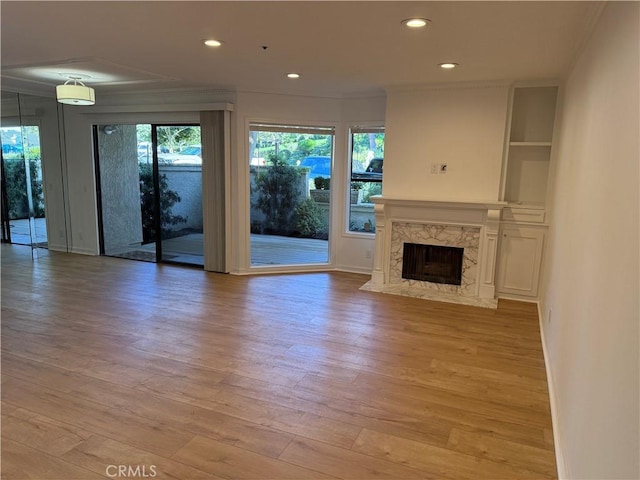 unfurnished living room with light wood-type flooring, ornamental molding, and a premium fireplace