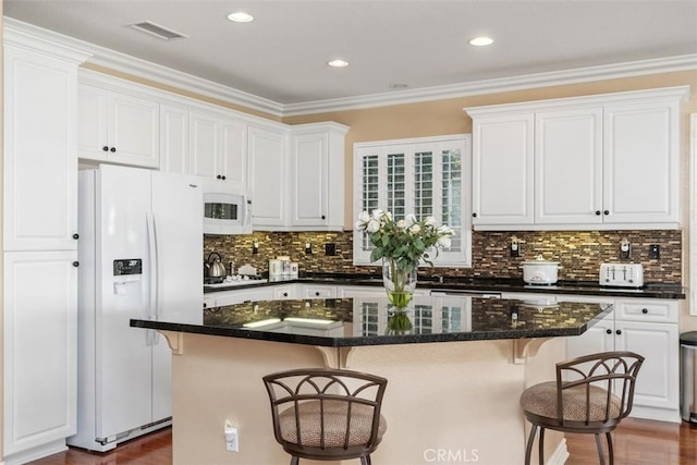 kitchen featuring visible vents, white appliances, a kitchen breakfast bar, and white cabinetry