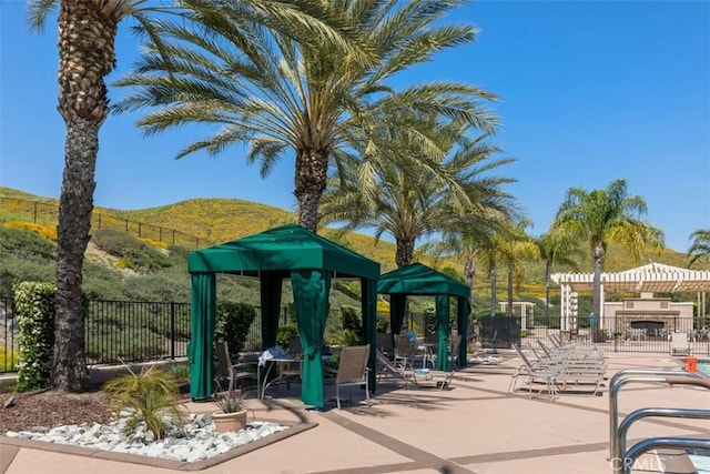 view of property's community featuring a mountain view, fence, a patio area, and a pergola