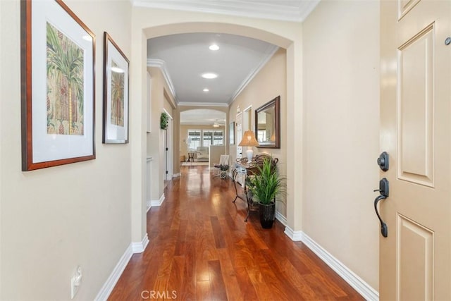 corridor with arched walkways, crown molding, baseboards, and wood finished floors