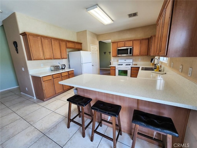 kitchen featuring light tile patterned floors, sink, white appliances, a breakfast bar, and kitchen peninsula