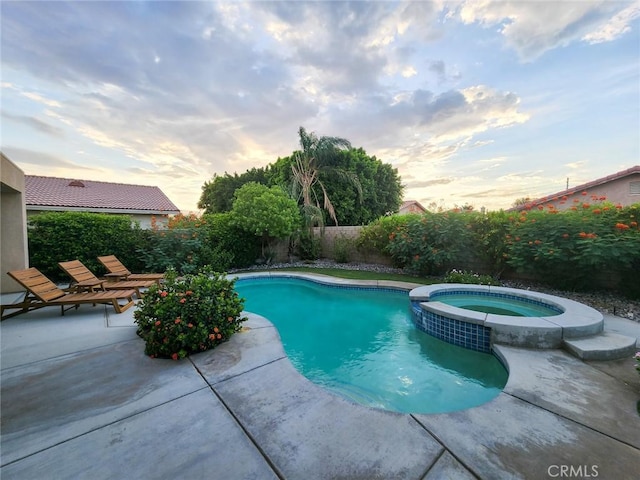 pool at dusk with an in ground hot tub and a patio area