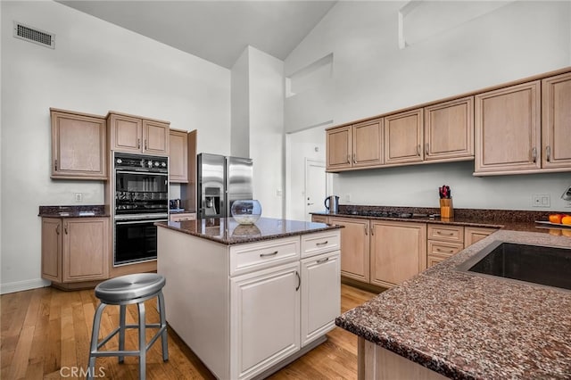 kitchen with a center island, light hardwood / wood-style flooring, high vaulted ceiling, stainless steel fridge, and black double oven