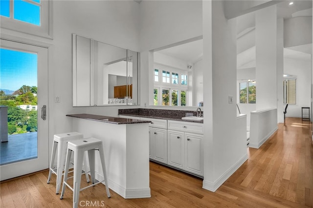 kitchen with kitchen peninsula, a kitchen bar, light wood-type flooring, sink, and white cabinetry