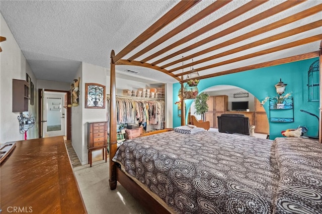 bedroom with a spacious closet, a textured ceiling, light colored carpet, and a closet