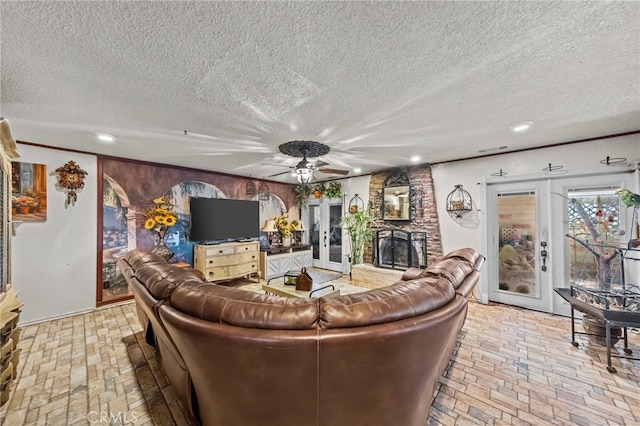 living room featuring a stone fireplace, french doors, a textured ceiling, and ceiling fan