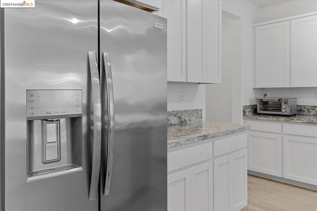 kitchen with stainless steel fridge, light stone counters, light hardwood / wood-style floors, and white cabinetry