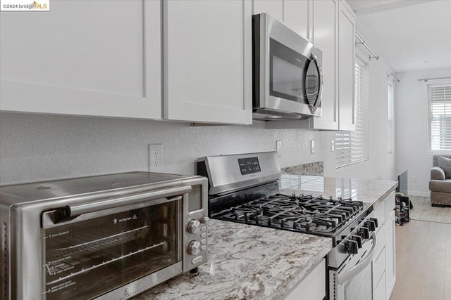 kitchen with white cabinets, appliances with stainless steel finishes, light hardwood / wood-style flooring, and light stone counters