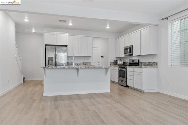 kitchen featuring white cabinetry, stainless steel appliances, light stone counters, light hardwood / wood-style floors, and a center island with sink