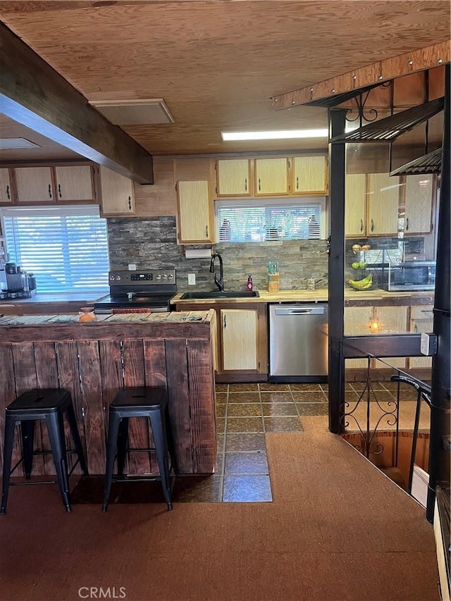 kitchen with decorative backsplash, appliances with stainless steel finishes, sink, beam ceiling, and a breakfast bar area