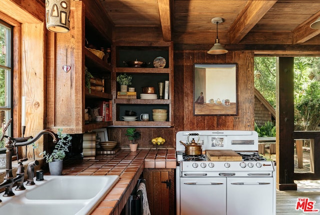 kitchen featuring tile countertops, sink, white range with gas cooktop, decorative light fixtures, and white cabinetry