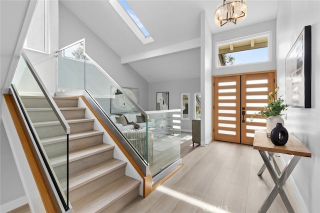 foyer featuring a chandelier, light hardwood / wood-style floors, high vaulted ceiling, and a skylight