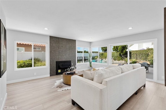 living room featuring a tiled fireplace, plenty of natural light, and light wood-type flooring