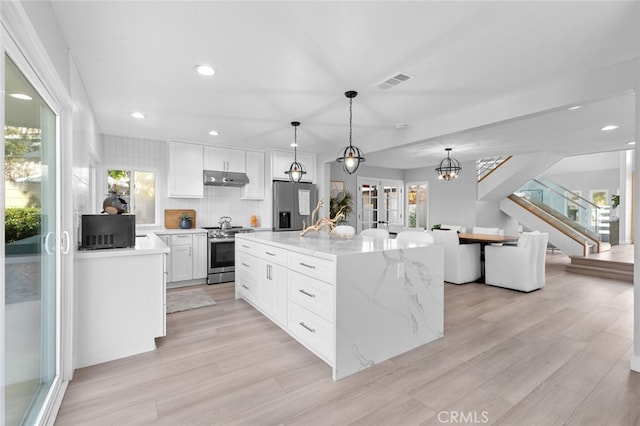 kitchen featuring stainless steel appliances, a center island, decorative light fixtures, light wood-type flooring, and white cabinets