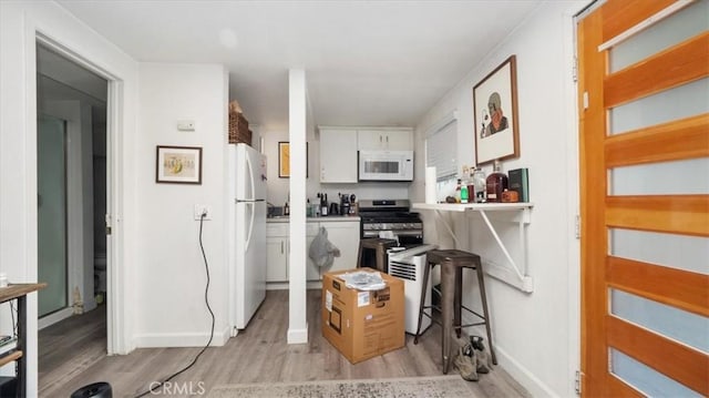 kitchen featuring baseboards, white cabinets, light wood finished floors, and white appliances