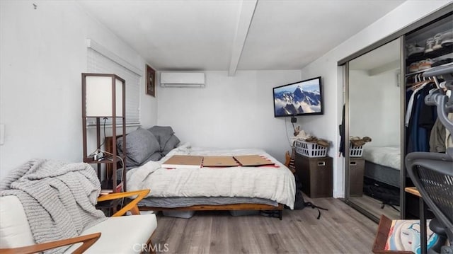bedroom with a closet, a wall mounted air conditioner, wood finished floors, and beam ceiling