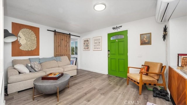 living area with baseboards, a barn door, light wood-style flooring, and a wall unit AC