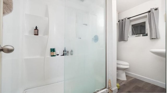 bathroom with baseboards, a stall shower, toilet, and wood finished floors