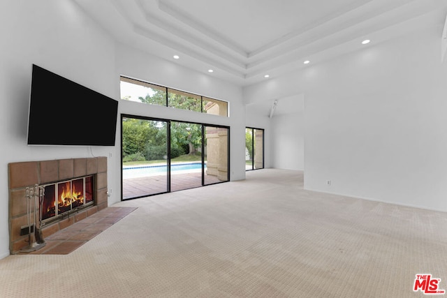 unfurnished living room with light colored carpet, a tile fireplace, and a high ceiling