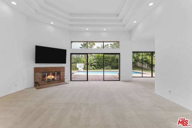 unfurnished living room featuring a raised ceiling, a tiled fireplace, light carpet, and a high ceiling