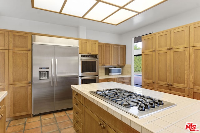 kitchen with tile countertops, decorative backsplash, light tile patterned flooring, and appliances with stainless steel finishes