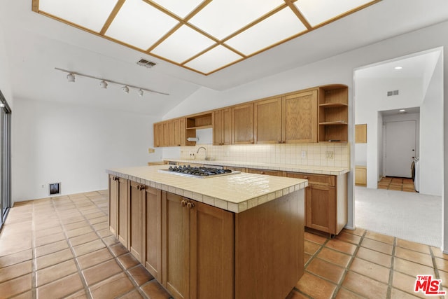 kitchen with decorative backsplash, stainless steel gas cooktop, tile countertops, a kitchen island, and lofted ceiling