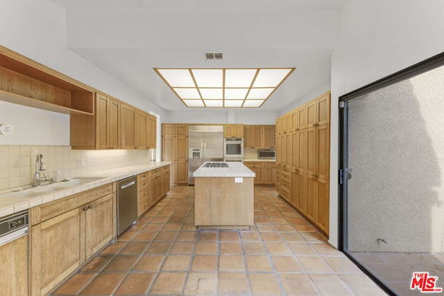 kitchen featuring sink, decorative backsplash, tile counters, a kitchen island, and stainless steel appliances