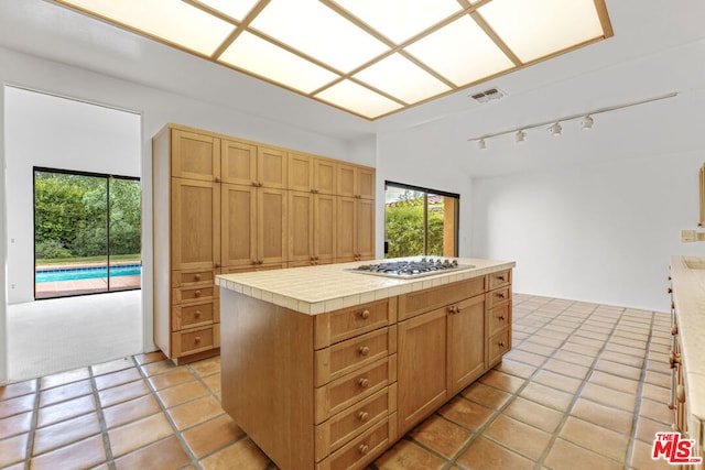 kitchen with stainless steel gas stovetop, tile counters, a center island, and light tile patterned flooring