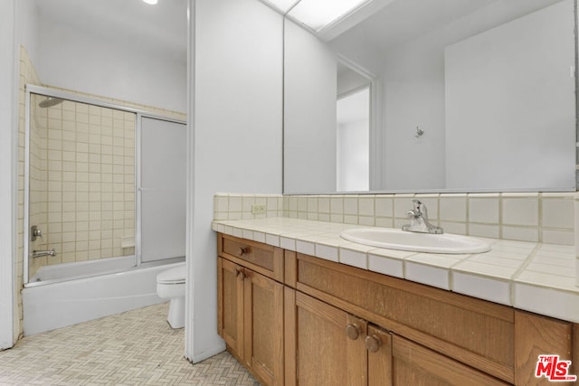 full bathroom with vanity, backsplash, toilet, and bath / shower combo with glass door