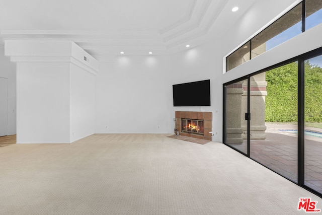 unfurnished living room featuring carpet, a raised ceiling, a fireplace, and a high ceiling