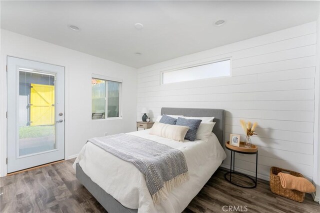 bedroom with multiple windows, wooden walls, and dark hardwood / wood-style floors