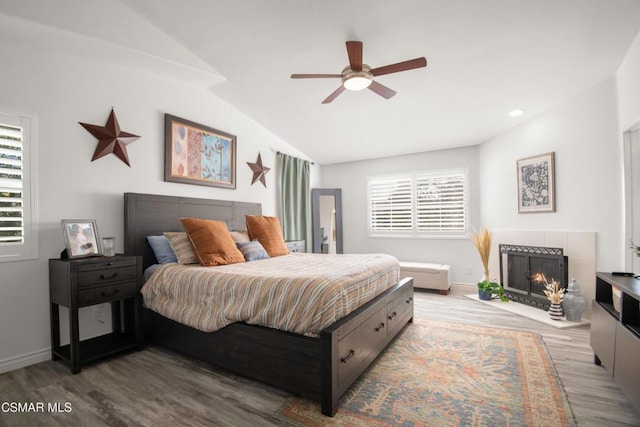 bedroom with a tile fireplace, light wood-type flooring, ceiling fan, and lofted ceiling