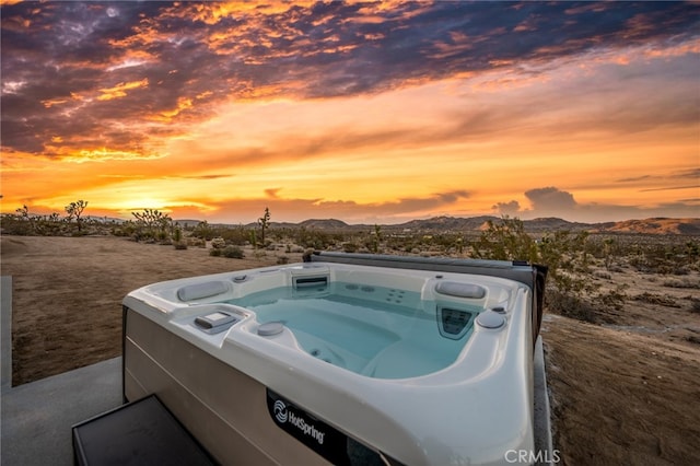 pool at dusk with a mountain view and a hot tub