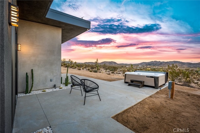 patio terrace at dusk featuring a hot tub and a mountain view