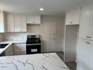 kitchen featuring hardwood / wood-style flooring, light stone countertops, white cabinetry, and stainless steel gas range