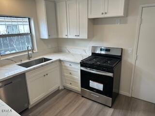 kitchen with light wood-type flooring, light stone counters, stainless steel appliances, sink, and white cabinets