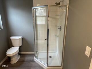 bathroom featuring hardwood / wood-style flooring, toilet, and a shower with shower door