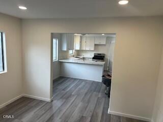 kitchen with white cabinets, dark hardwood / wood-style floors, kitchen peninsula, and stainless steel range