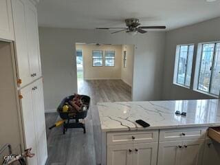 kitchen with light stone counters, white cabinetry, light wood-type flooring, and a wealth of natural light