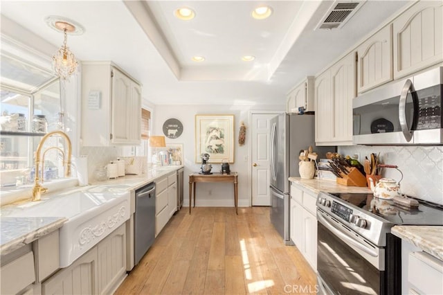 kitchen with backsplash, hanging light fixtures, light hardwood / wood-style flooring, appliances with stainless steel finishes, and white cabinetry