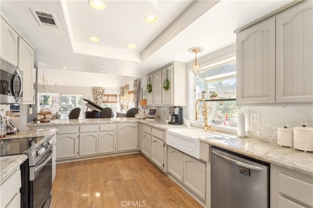 kitchen with stainless steel appliances, backsplash, pendant lighting, light hardwood / wood-style floors, and a tray ceiling