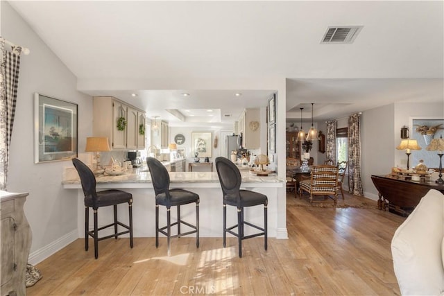 kitchen with a notable chandelier, a breakfast bar, light hardwood / wood-style floors, and kitchen peninsula