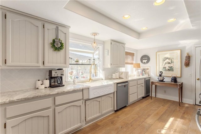 kitchen with a raised ceiling, dishwasher, light hardwood / wood-style floors, and sink