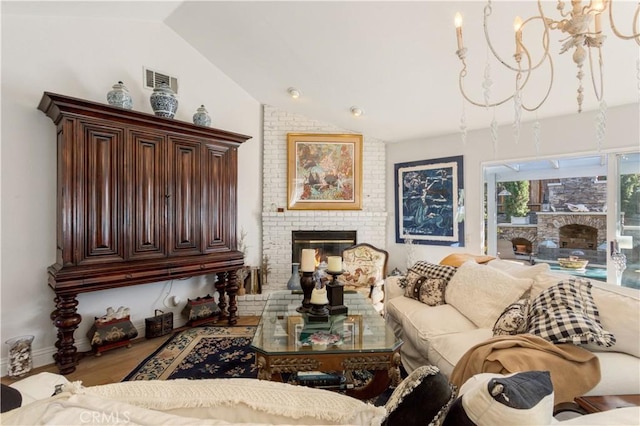 living room with a brick fireplace, an inviting chandelier, vaulted ceiling, and wood-type flooring