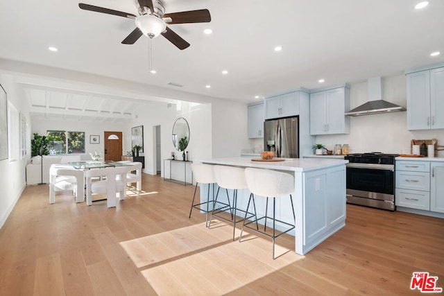 kitchen featuring appliances with stainless steel finishes, a kitchen island, white cabinetry, wall chimney range hood, and light hardwood / wood-style floors