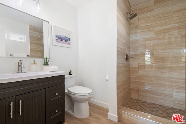 bathroom featuring toilet, vanity, tiled shower, and hardwood / wood-style flooring